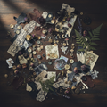 Mixed media junk journal kit flat lay with leather scraps, lace, buttons, dried flowers and themed ephemera on dark wooden surface